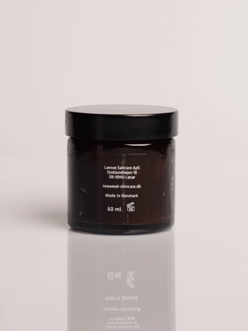 Brun glaskrukke med sort låg, hudplejecreme 60 ml fra dansk seaweed-skincare, reflekteret på blank overflade