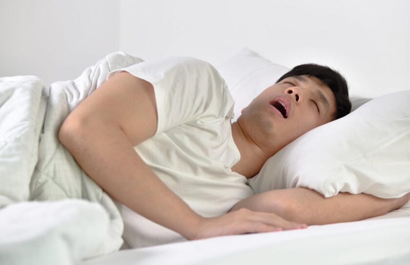 Mand sover på siden med åben mund på hvidt sengetøj