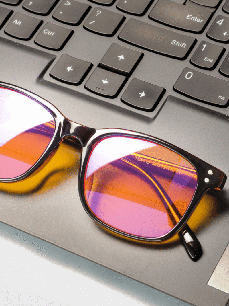 Solbriller med pink-orange spejlglas på laptop-tastatur nær piletaster