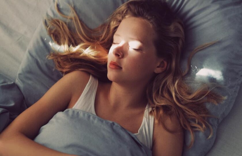 Ung kvinde sover, første morgenlys skinner på hendes ansigt under blåt sengetøj