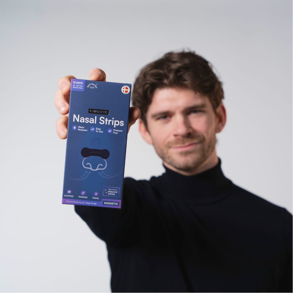 Mand i sort trøje holder blå æske med Magnetic Nasal Strips, næseillustration og produkttekst i fokus