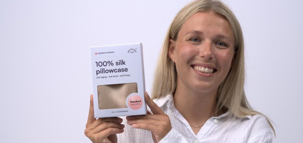 Smilende kvinde holder æske med 100% silkepudebetræk i beige, standardstørrelse